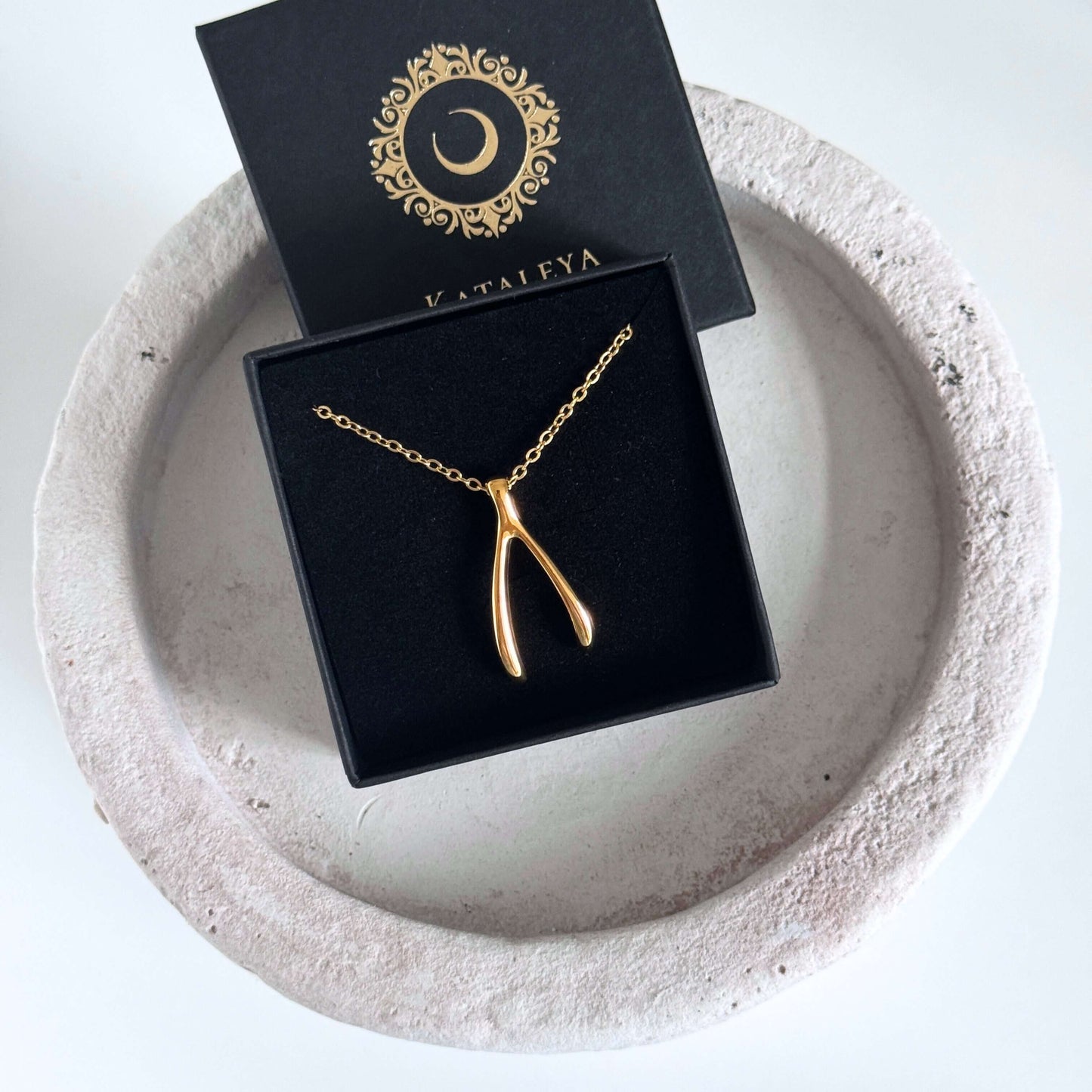 Gold Wishbone Pendant Necklace displayed in a black box on a round stone tray.