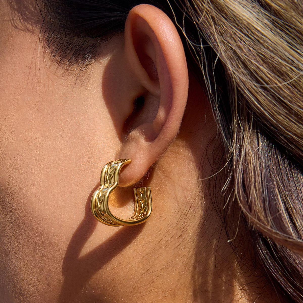 Close-up of a woman's ear adorned with chunky gold heart earrings, showcasing their elegant design and shine.
