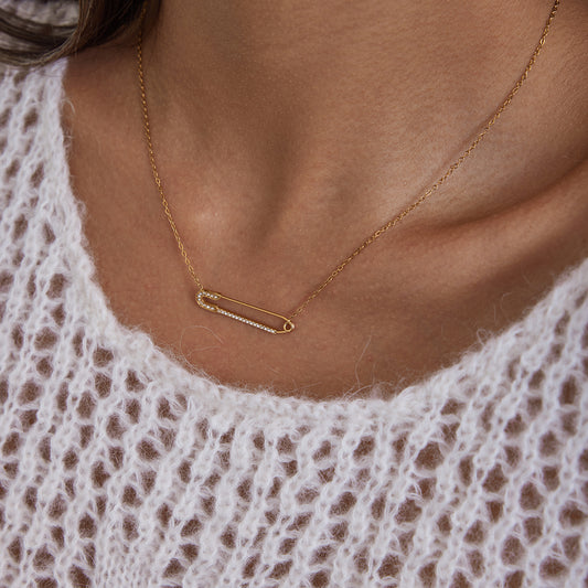 Close-up of a woman wearing a gold safety pin necklace on a textured white sweater.