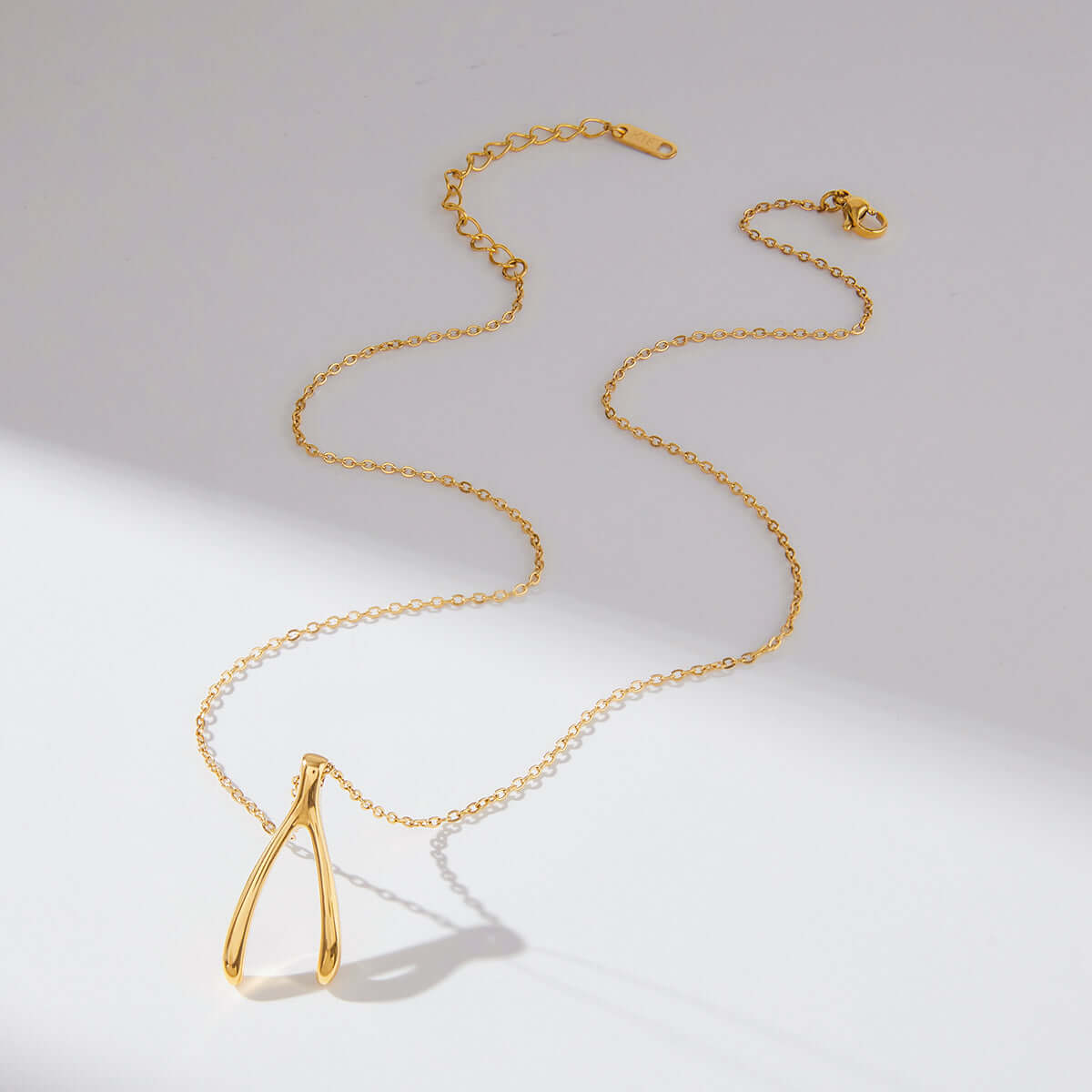 Gold Wishbone Pendant Necklace displayed elegantly on a smooth surface with a dainty gold chain.